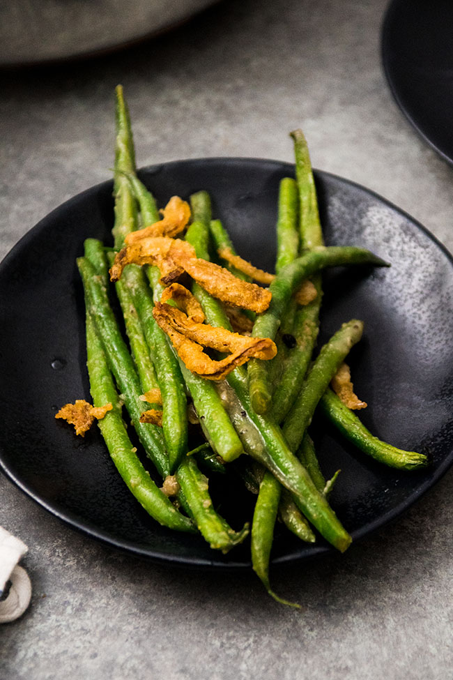 Green beans topped with fried onions on a black plate.