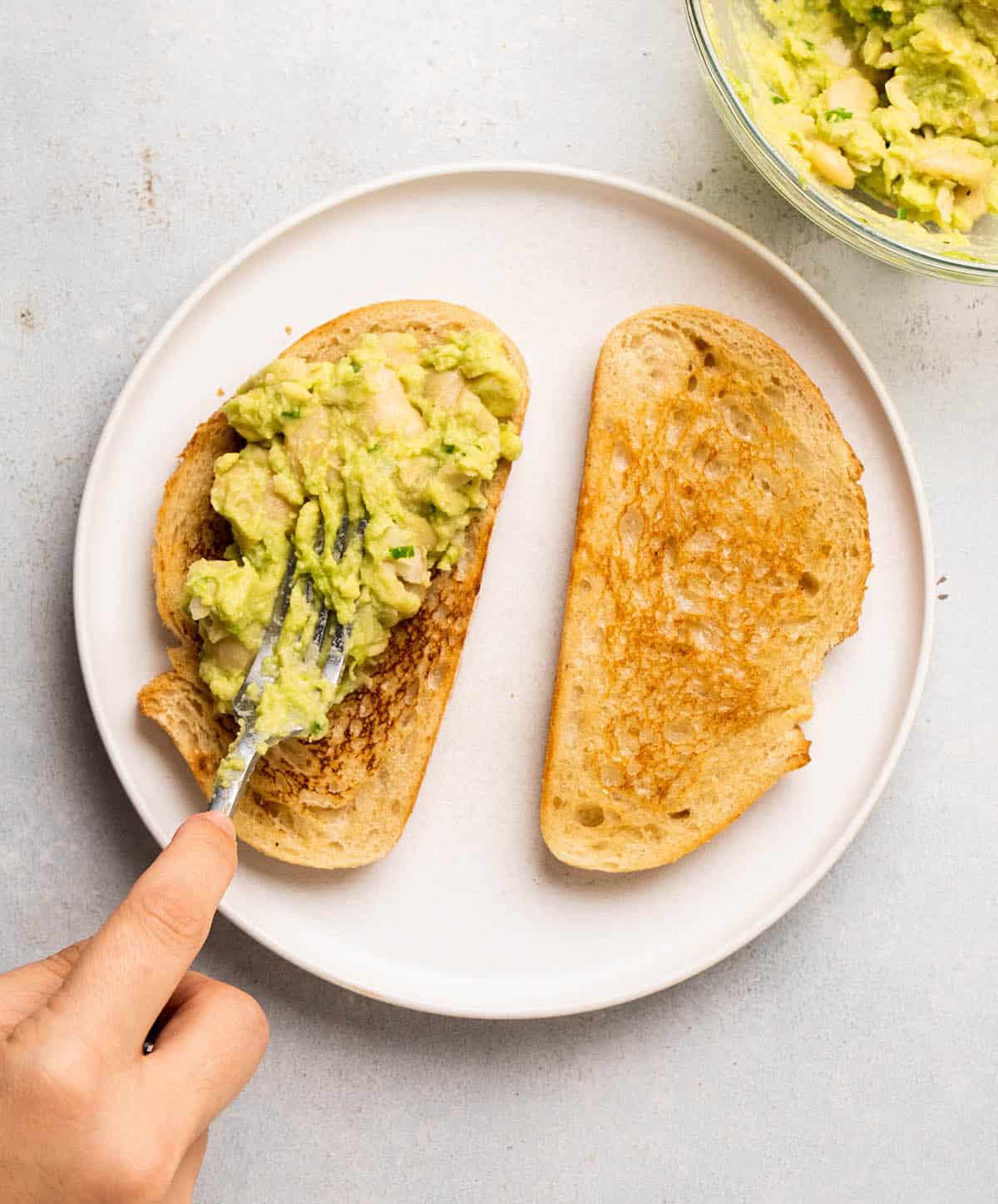 Spreading avocado and beans over toast with a fork.