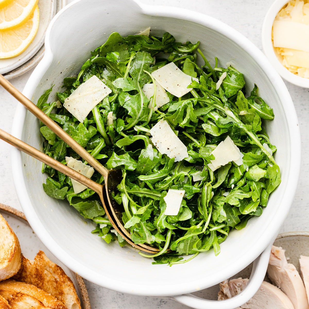 Arugula salad in a large white bowl with two serving forks.