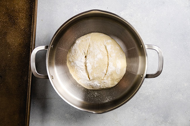 Uncooked bread dough, shaped into a round loaf, sitting in a stainless steel pot.