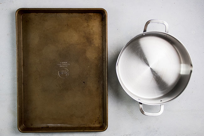 Baking sheet next to a stainless steel pot on a white table.