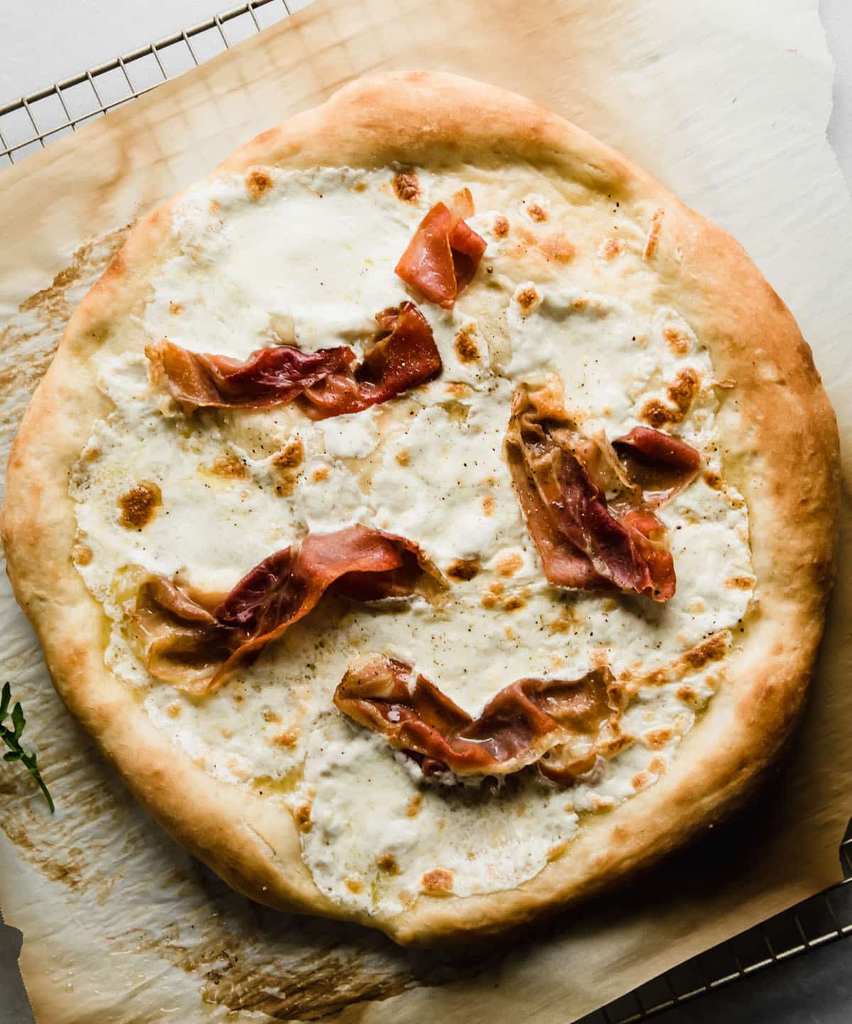 Pizza with crispy prosciutto, sitting on a wire cooling rack with a piece of parchment paper.