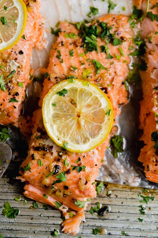 Baked steelhead trout portions topped with parsley and lemon slices.
