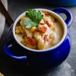 White chowder in a small blue bowl topped with bacon and fresh parsley.