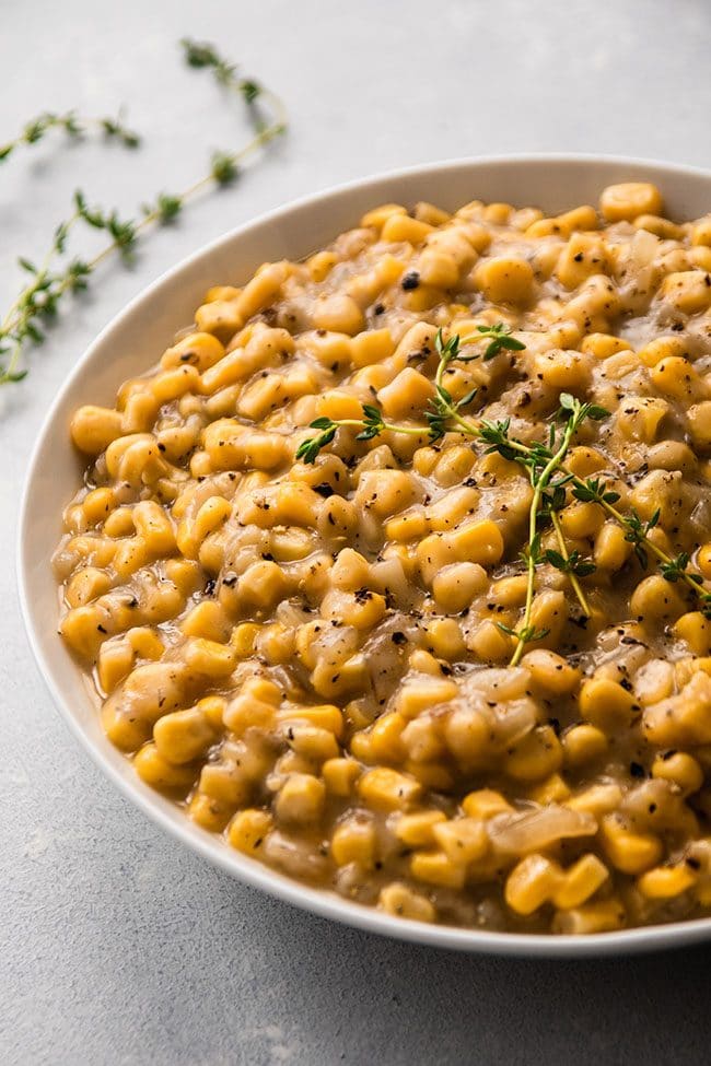 Creamed corn topped with fresh thyme sprigs in a white bowl.