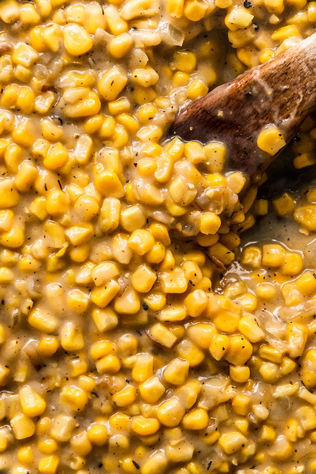 Wooden spoon stirring creamed corn.