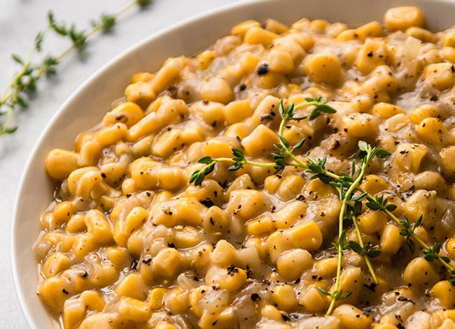 Creamed corn in a white bowl topped with fresh thyme.