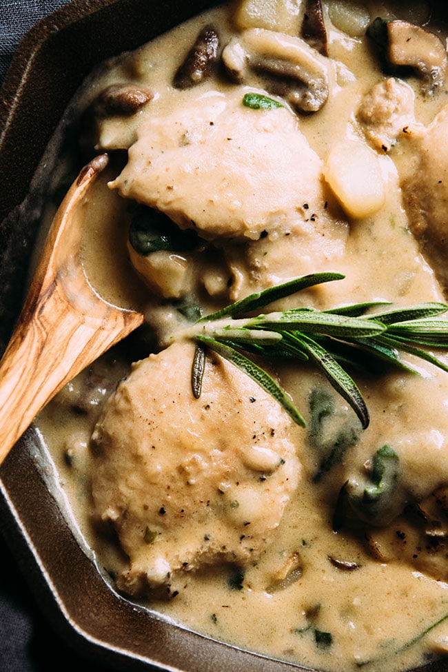 Wooden spoon lifting a piece of chicken out of the skillet.