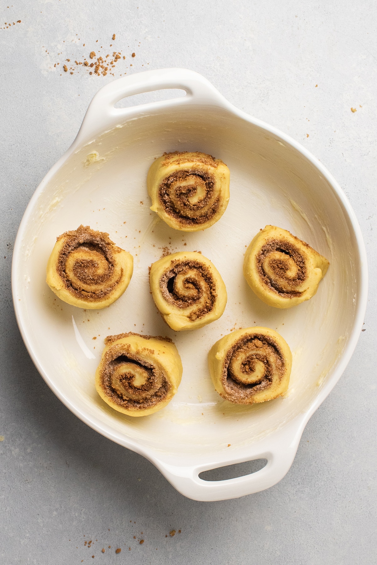 Six cinnamon rolls in a white dish before baking.