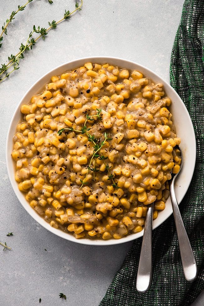 Creamed corn in a shallow white bowl with two spoons and a green napkin on the side.