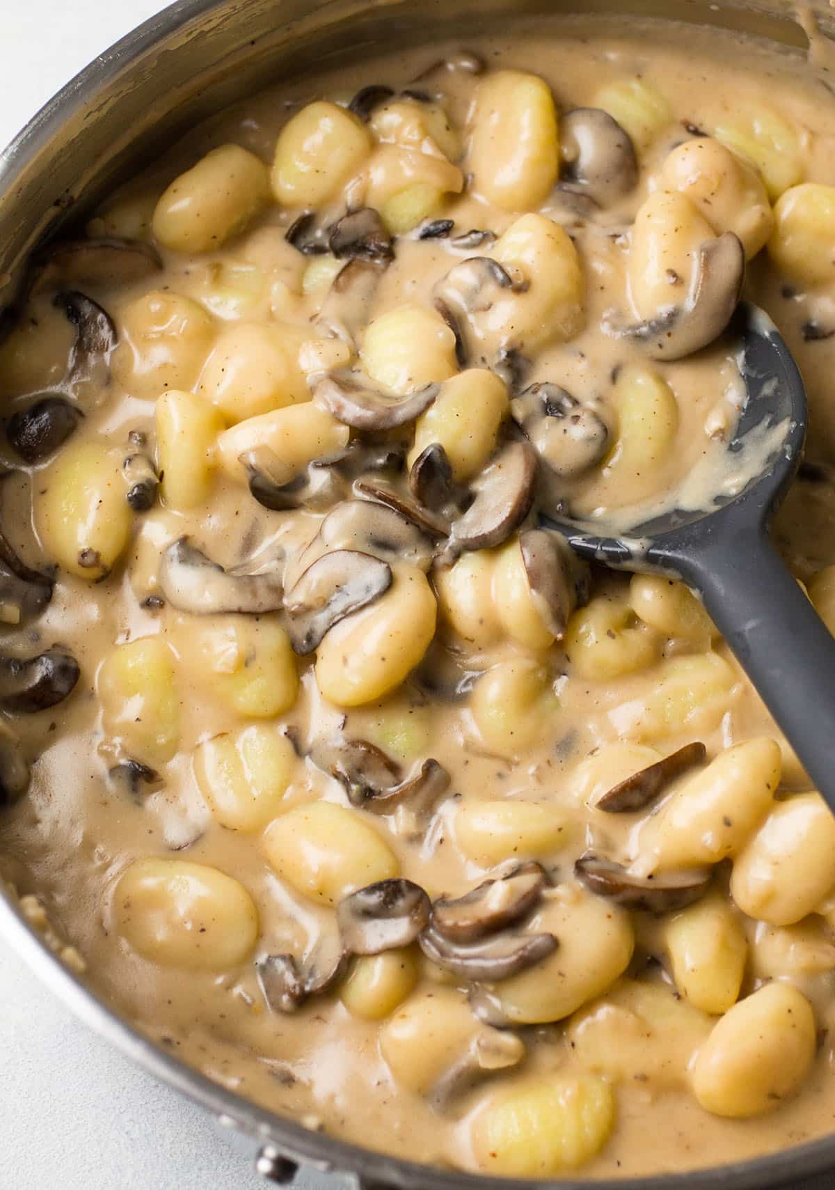 Black spoon stirring mushroom gnocchi in a large skillet.