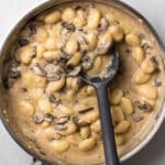 Black spoon stirring mushroom gnocchi in a large skillet.