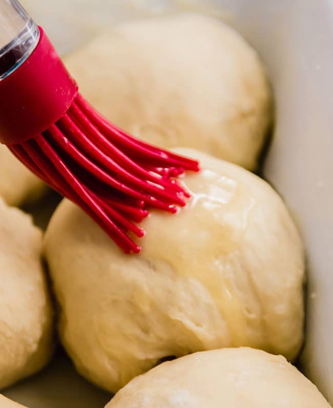 Red pastry brush brushing melted butter over bread dough.