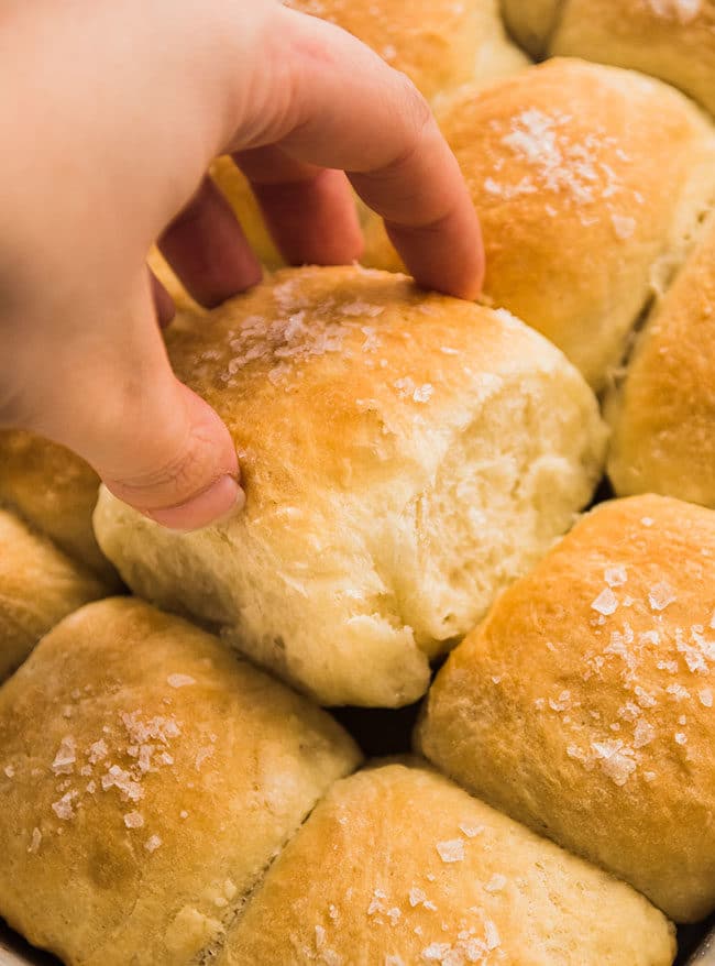 Woman\'s hand pulling a dinner roll out of a casserole dish.