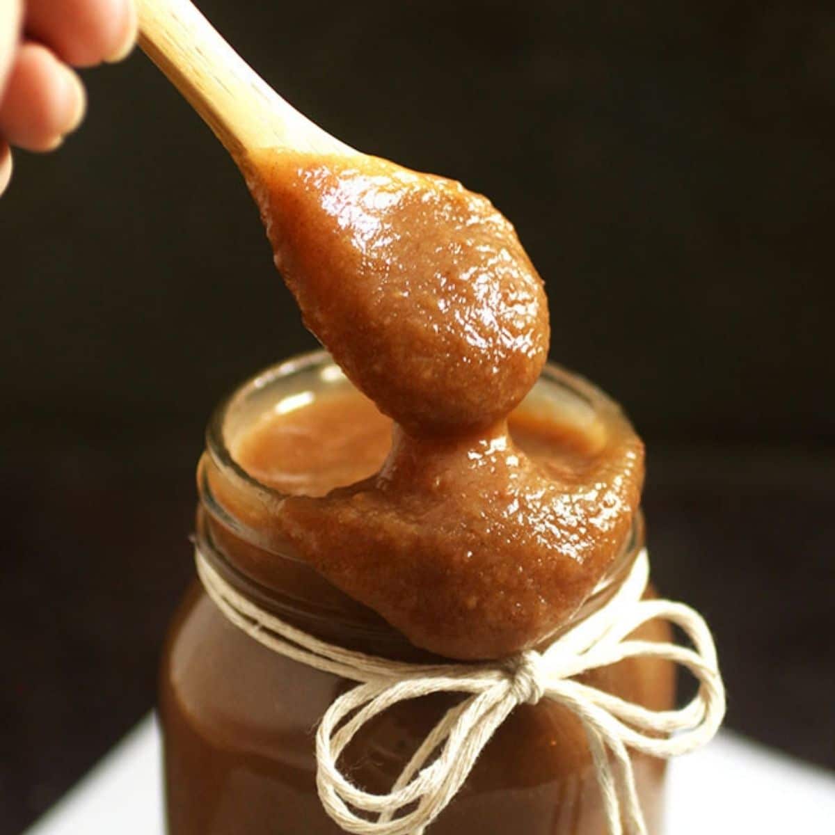 Wooden spoon drizzling apple butter into a mason jar.