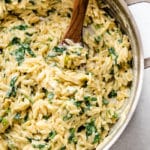 Wooden spoon stirring orzo and spinach in a silver pot.