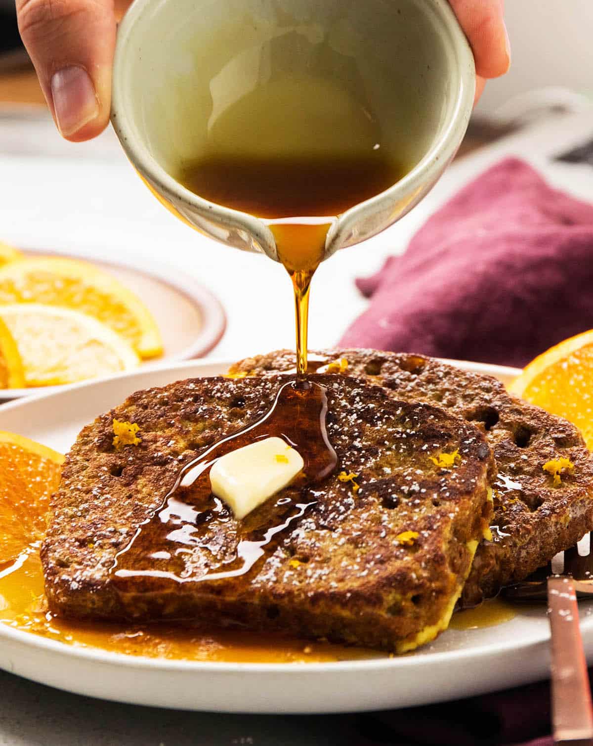 Pouring maple syrup over two slices of french toast.