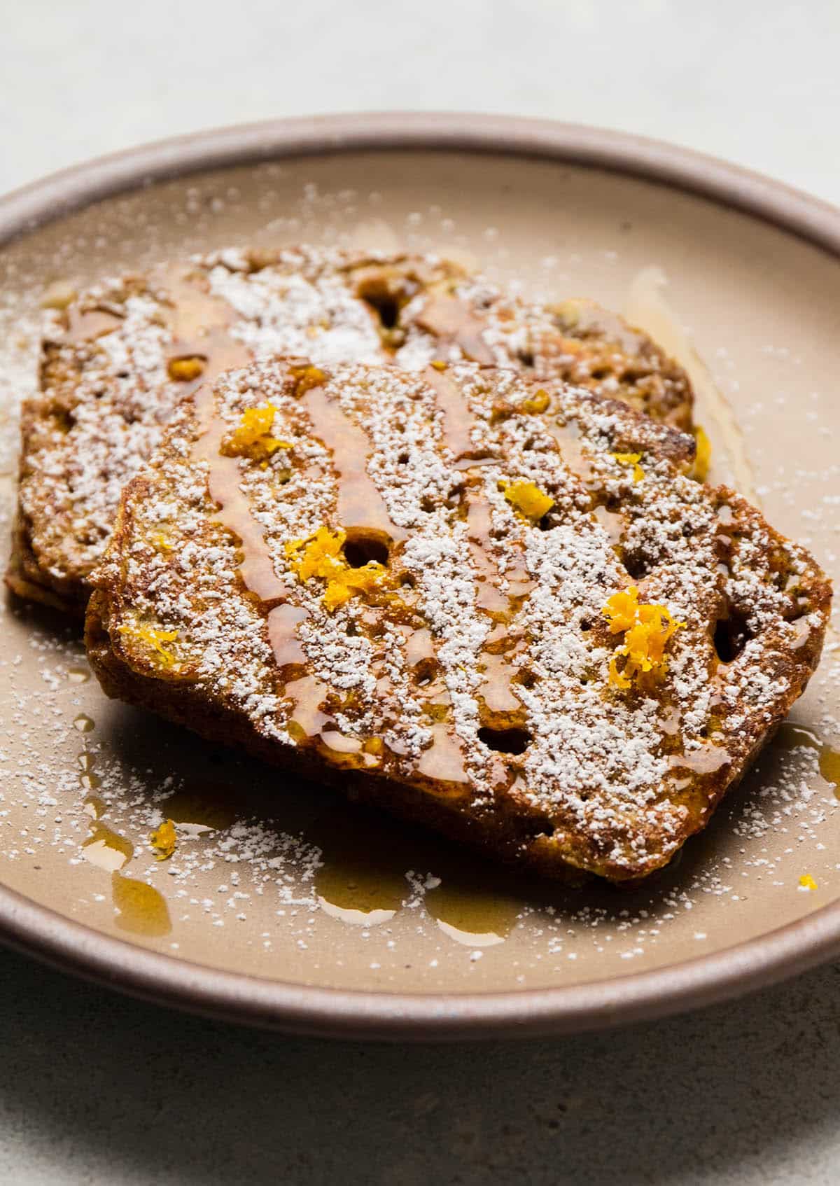 Two slices of french toast topped with powdered sugar and orange zest.