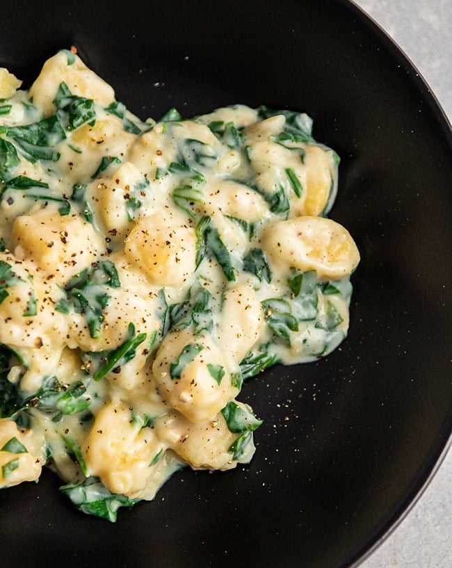 Gnocchi with cream sauce and spinach on a black plate.