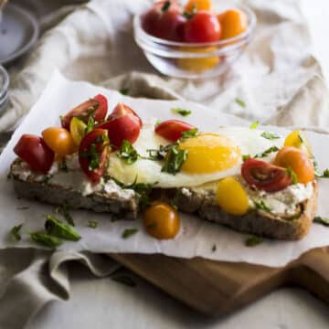 Sunny side up egg on toast with cherry tomatoes and chopped basil.