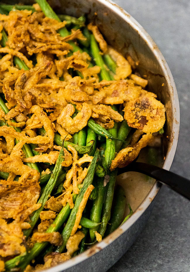 Black fork lifting green bean casserole out of a metal pan.