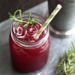 Blackberry whiskey lemonade in a mason jar filled with ice, topped with a striped paper straw and a sprig of fresh rosemary.