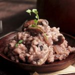 Light pink risotto on a dark wooden plate, topped with a sprig of fresh thyme.