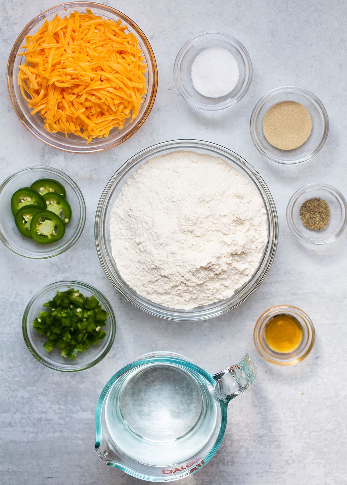 Jalapeno cheese bread ingredients, organized into individual glass bowls on a white table.