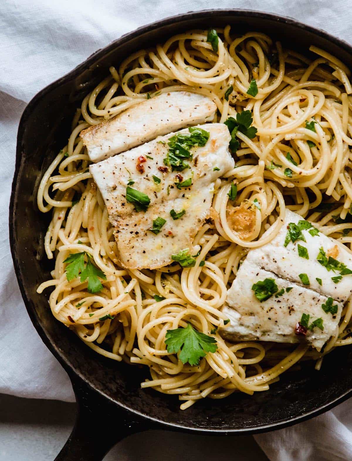 Cooked fish sitting on top of lemon spaghetti in a cast iron skillet.
