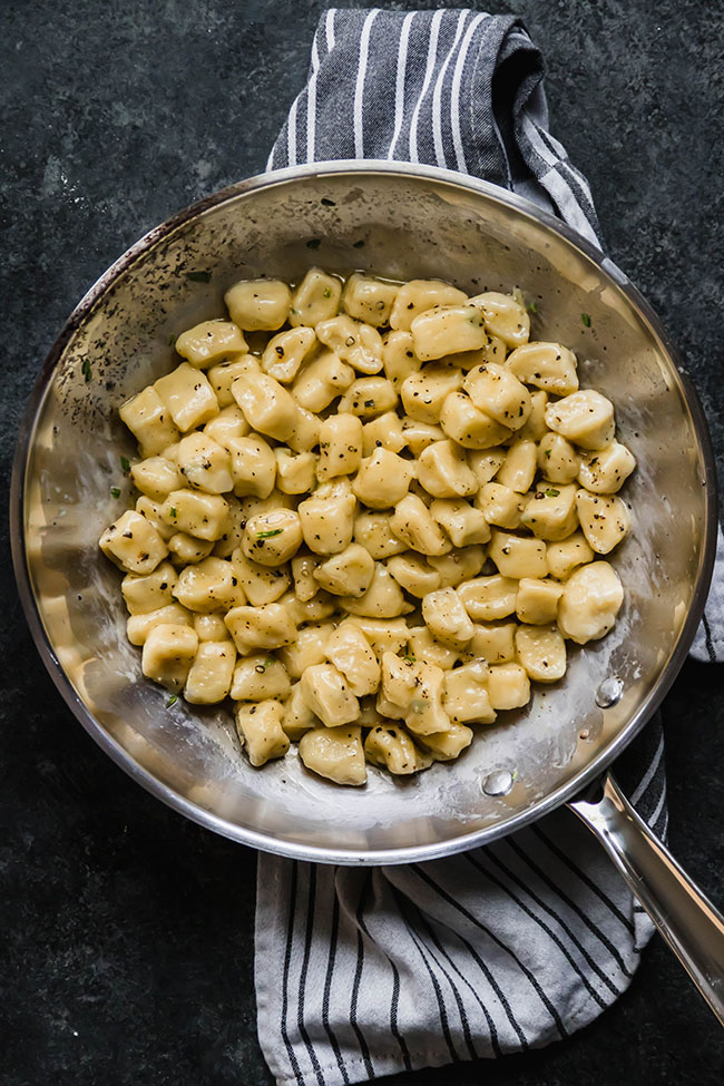 Cooked gnocchi tossed with butter and black pepper in a silver skillet.