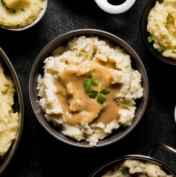 Several small bowls of mashed potatoes on a dark table with a variety of toppings like gravy, herbs, and melted butter.