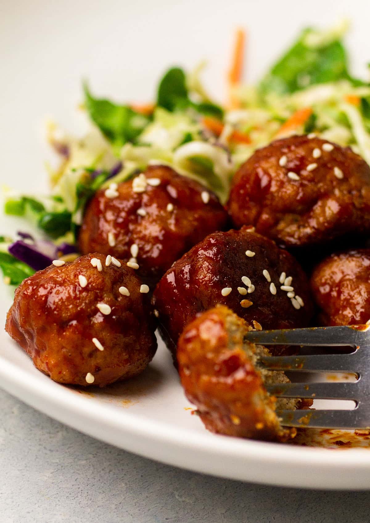 Meatballs with gochujang sauce on a plate with salad.