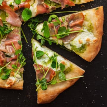 Pea shoot pizza slices on a black cutting board.