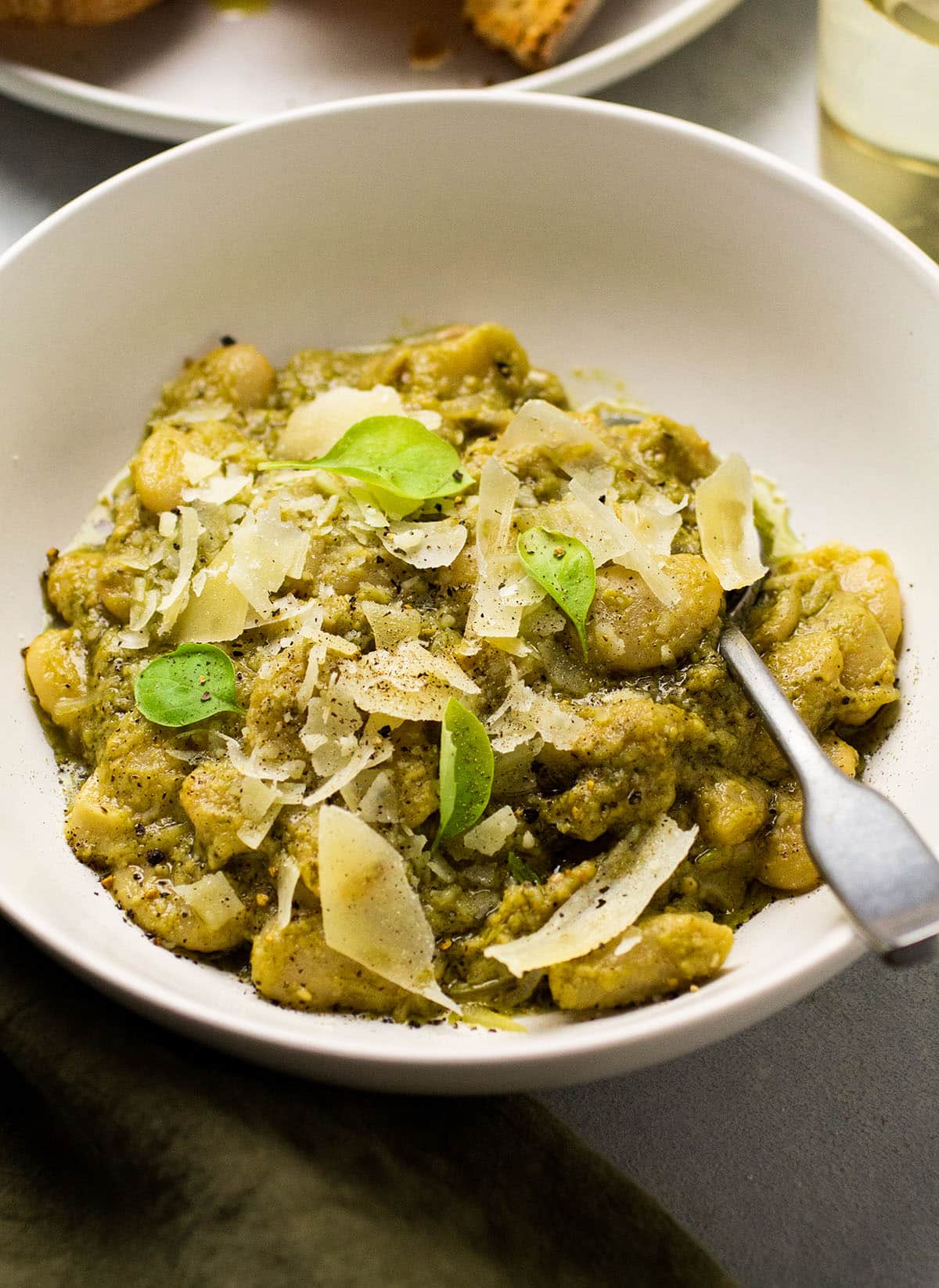 Pesto beans in a white bowl, topped with parmesan and fresh basil.