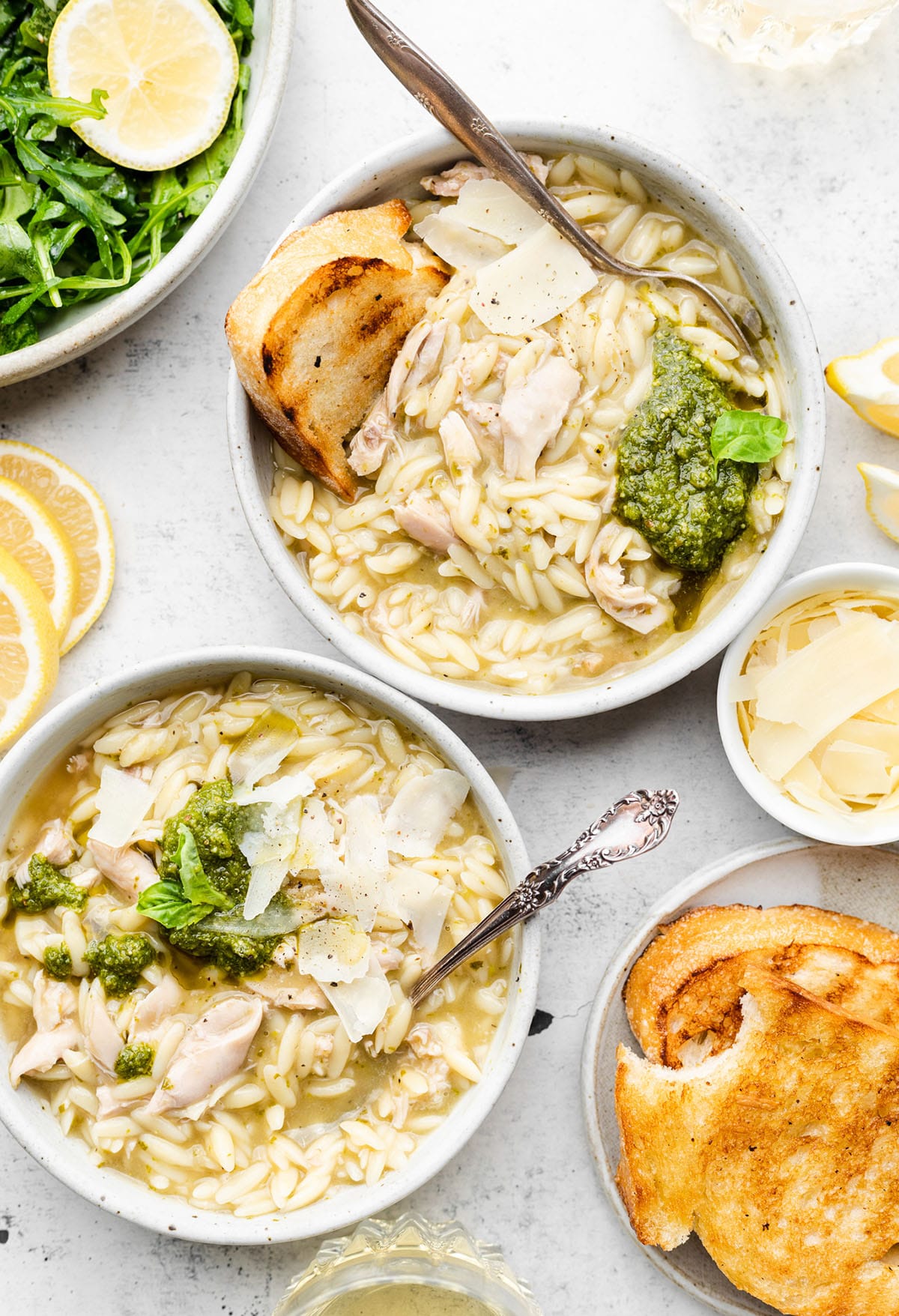 Two bowls of chicken soup, each with a silver spoon sticking out, next to a plate of toasted bread.