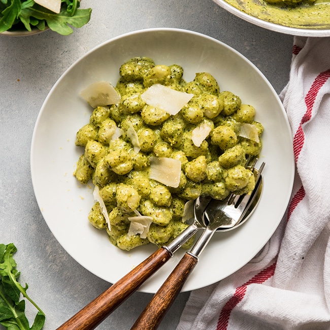 White bowl filled with gnocchi in a pesto sauce, topped with parmesan cheese.
