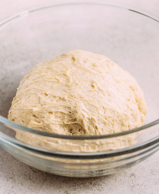 Pizza dough in a glass mixing bowl on a white background.