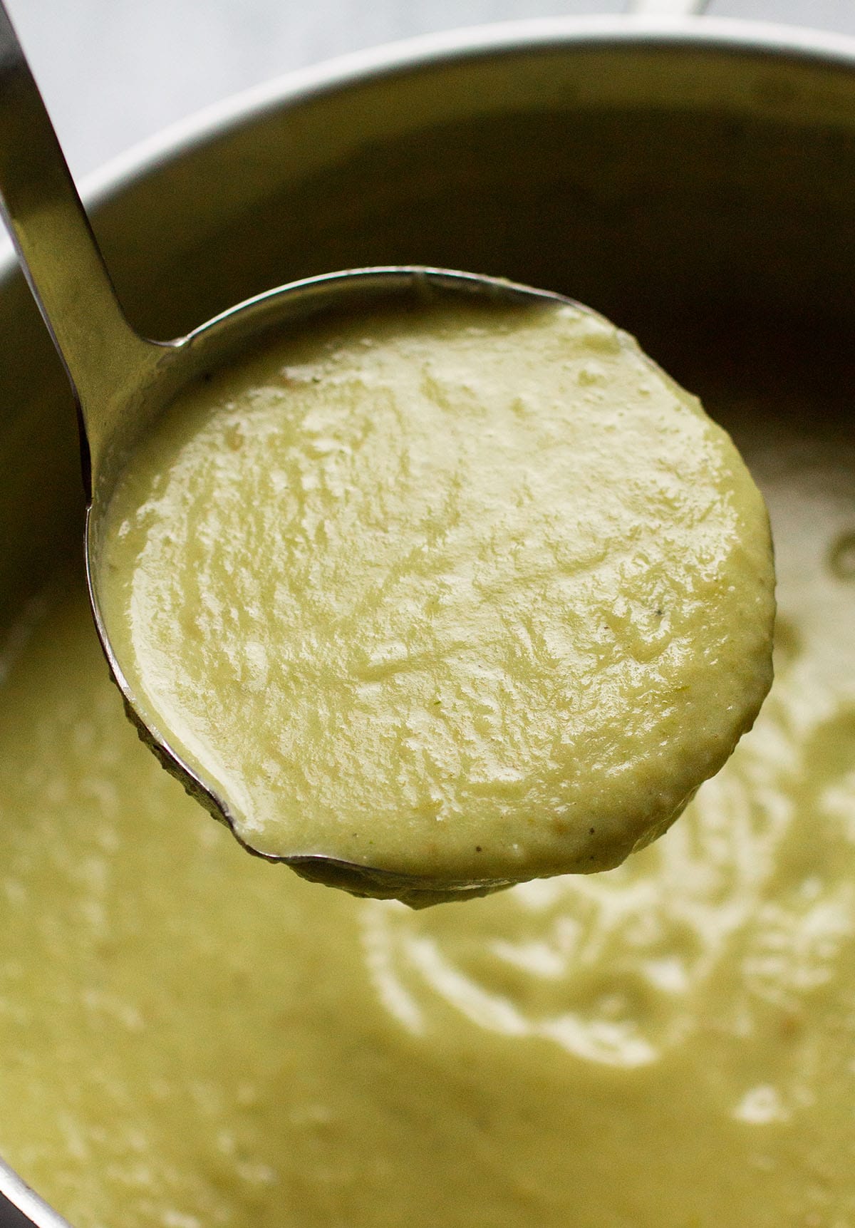 Silver ladle lifting a scoop of potato soup out of a large pot.