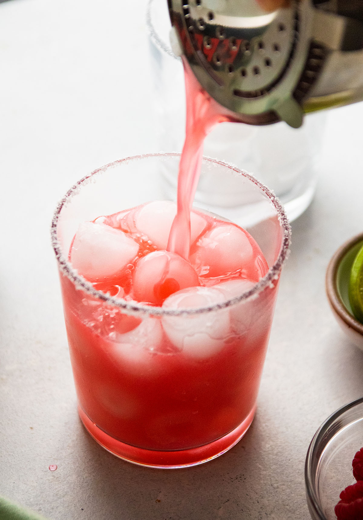 Silver cocktail shaker pouring a pink margarita into a short glass.