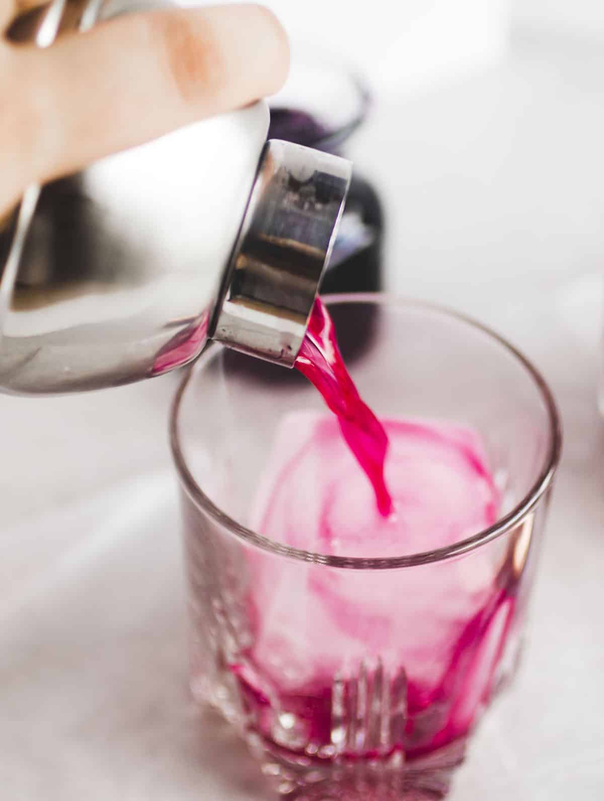 Pouring the cocktail into a glass full of ice with a metal cocktail shaker.