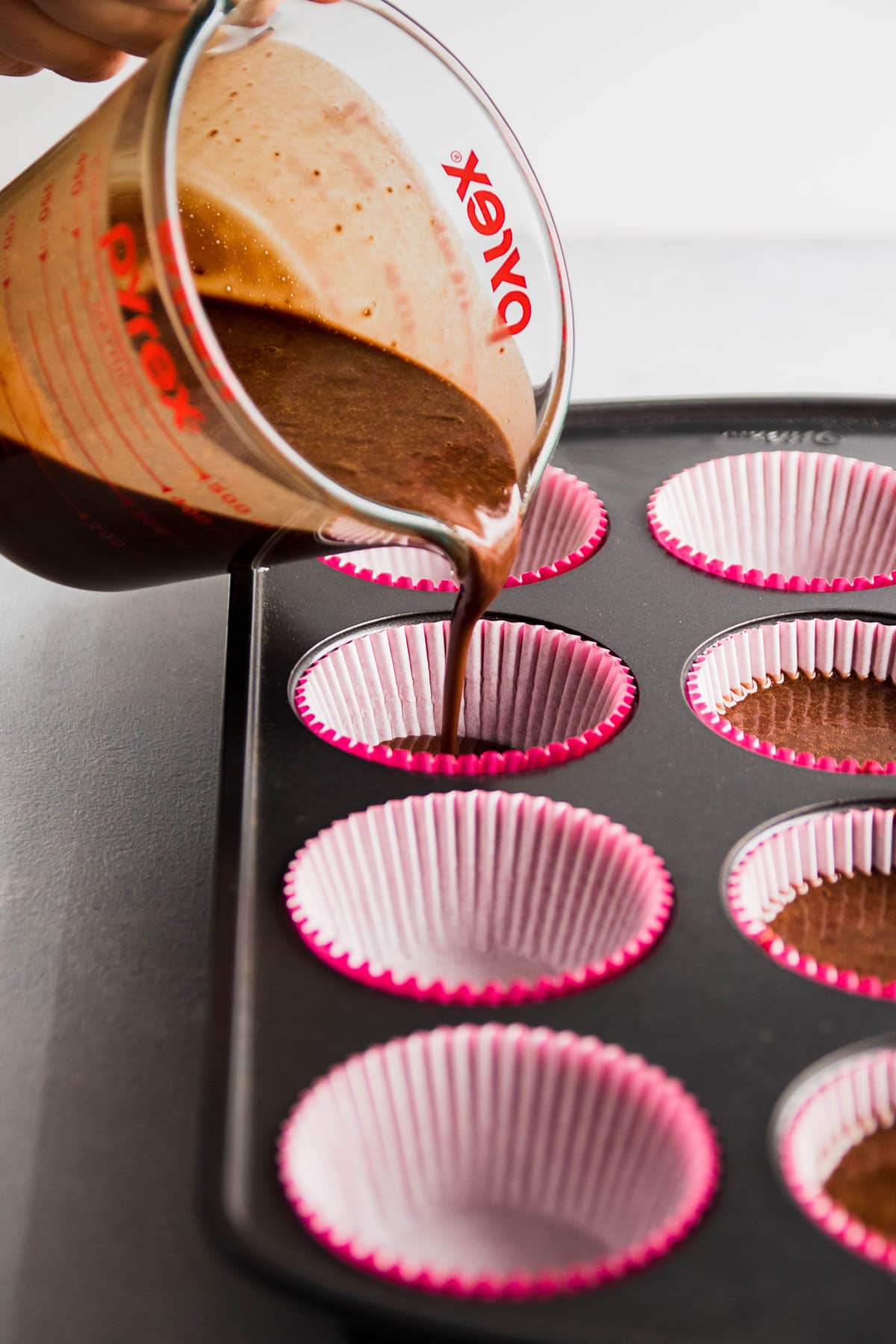 Pouring cupcake batter into liners with a small measuring cup.
