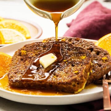 Pouring maple syrup over two slices of pumpkin bread french toast.