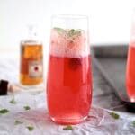 Raspberry spritzer in a champagne glass in front of a white background.