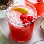 Margarita in a short glass, topped with fresh raspberries and a lime wedge.