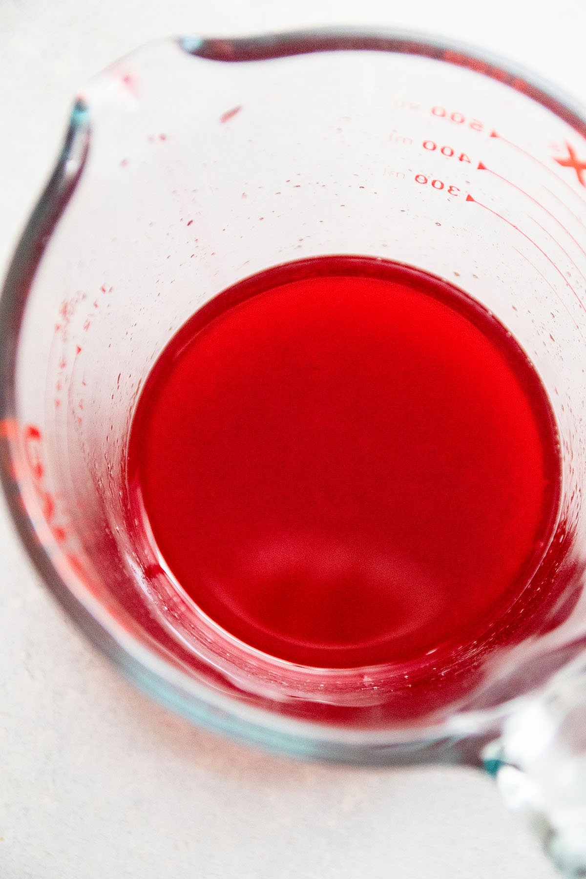 Looking into a glass measuring cup filled with pink raspberry syrup.