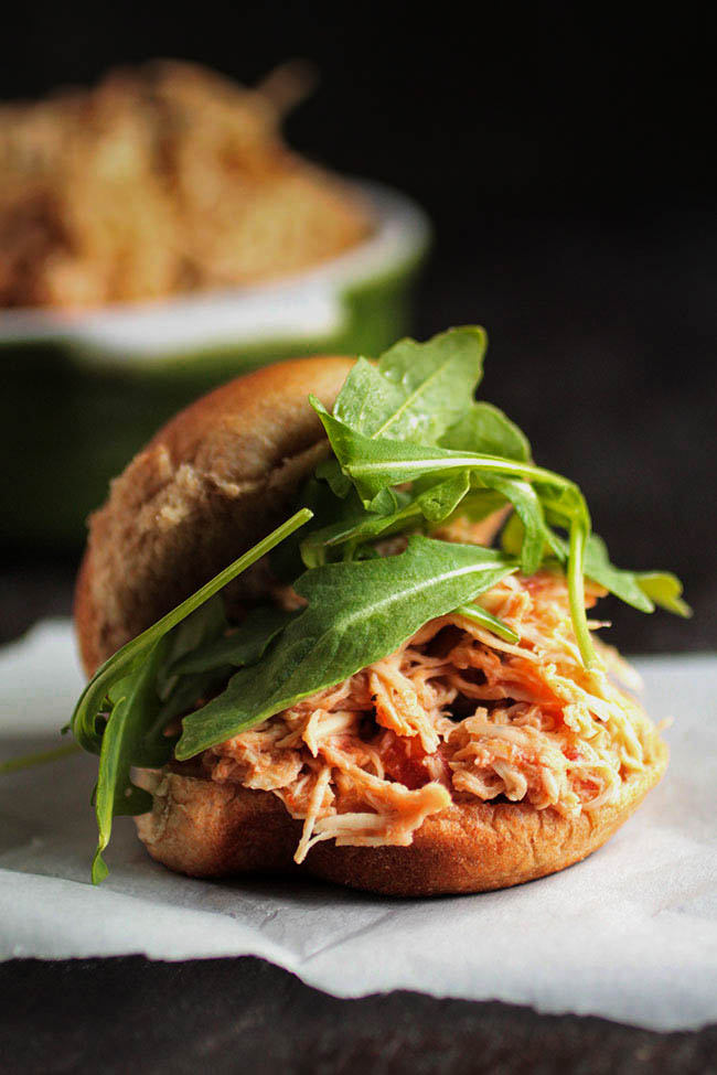 Sandwich roll with shredded chicken and arugula on a dark background.