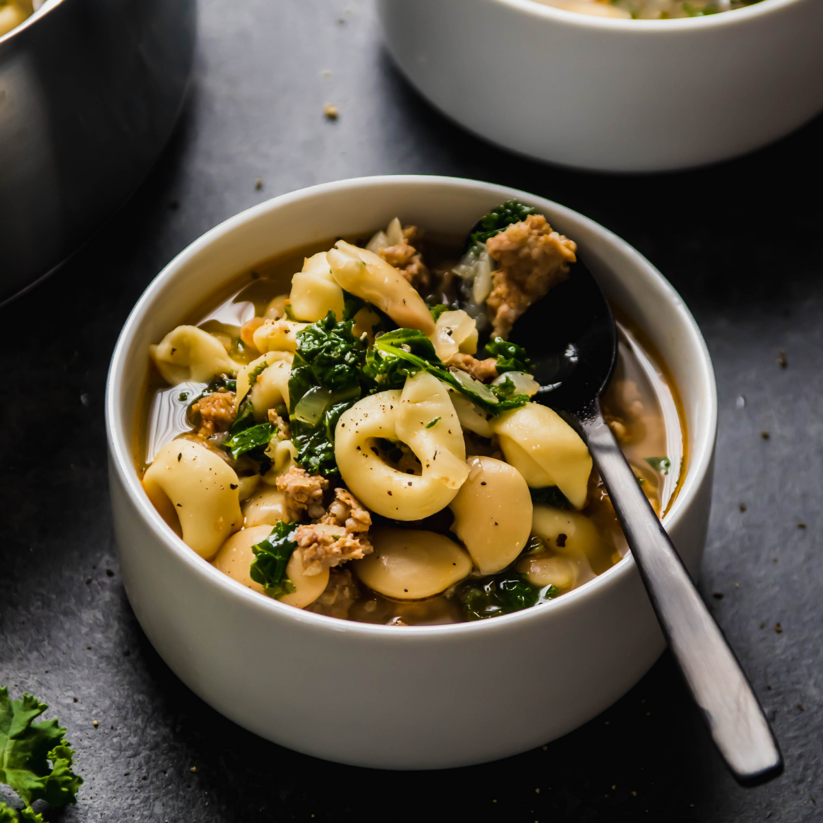 Tortellini soup with sausage and kale in a white bowl.
