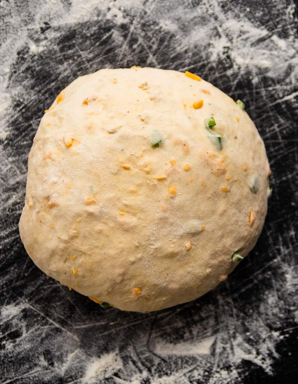 Jalapeno cheese dough, shaped into a round loaf on a black cutting board.