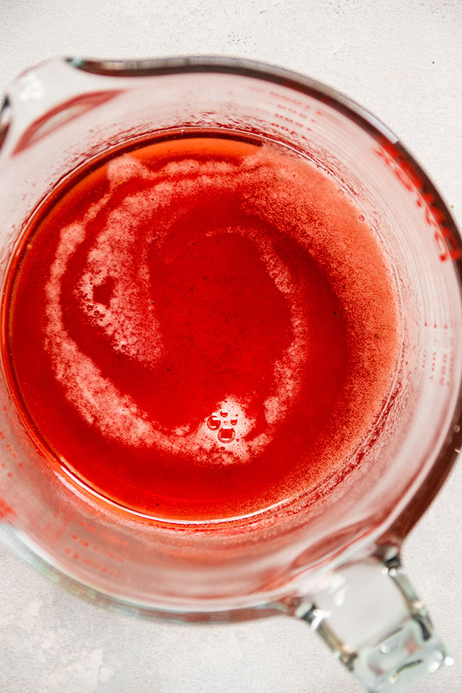 Looking into a glass measuring cup filled with bright pink strawberry thyme simple syrup.