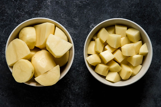 Two bowls on a black background, one filled with large potato pieces and the other filled with small potato pieces.